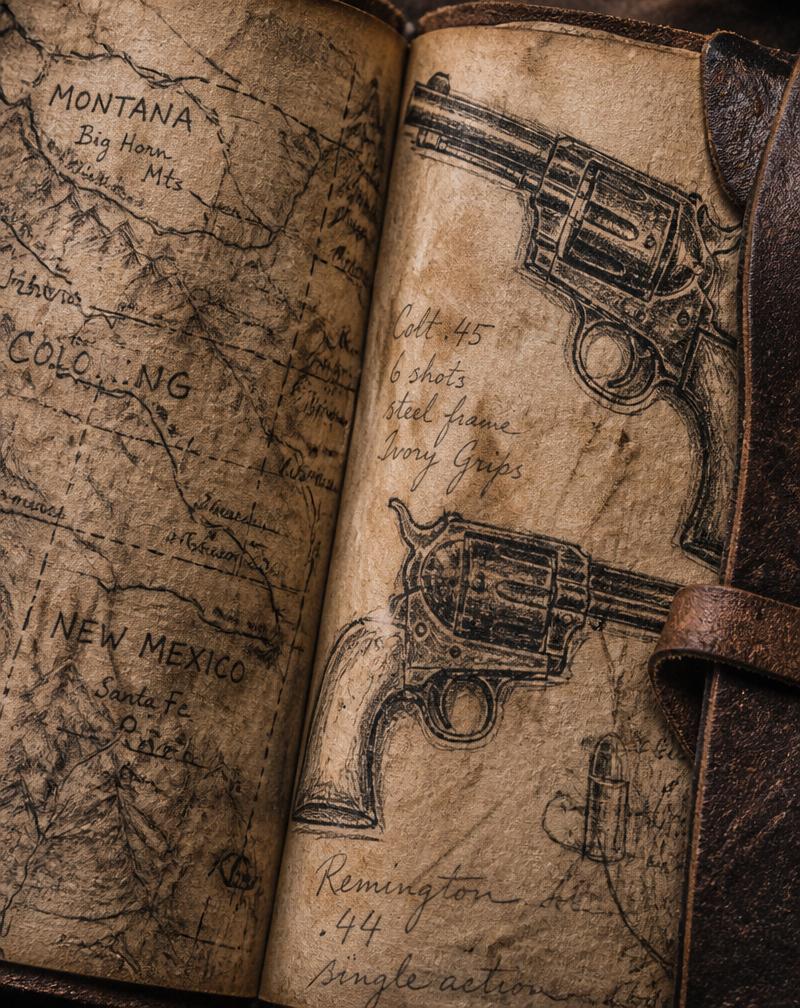 Weathered leather journal with hand-drawn maps of the American West and charcoal sketches of revolvers